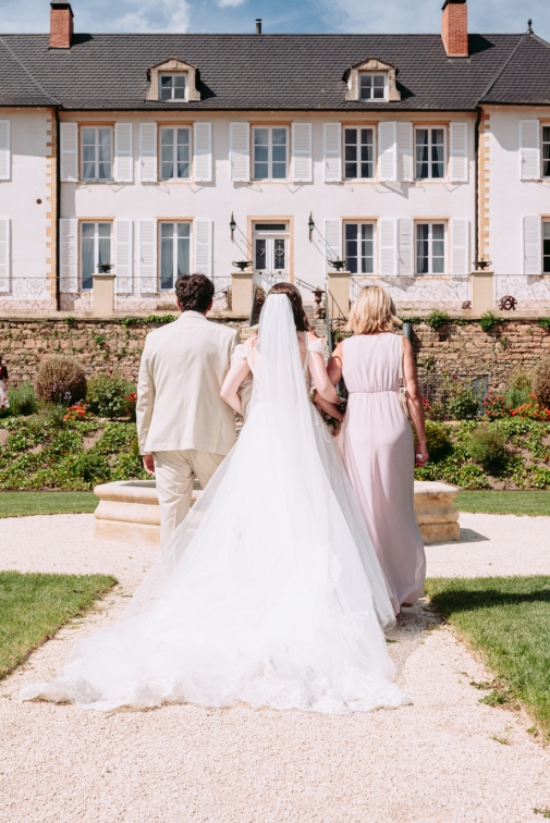 Une mariée de dos accompagnée par ses parents à la cérémonie